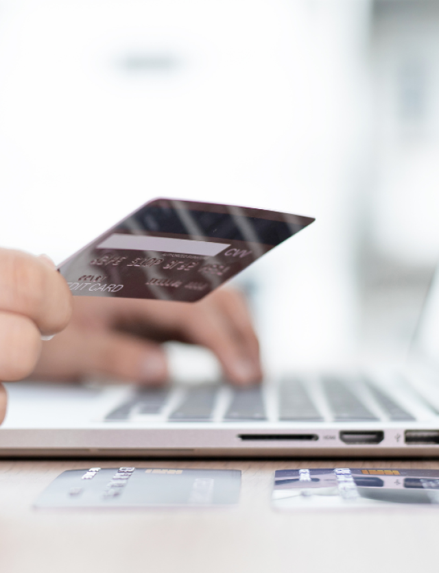 a hand holding a credit card above the laptop, about to make a payment for the online purchase.