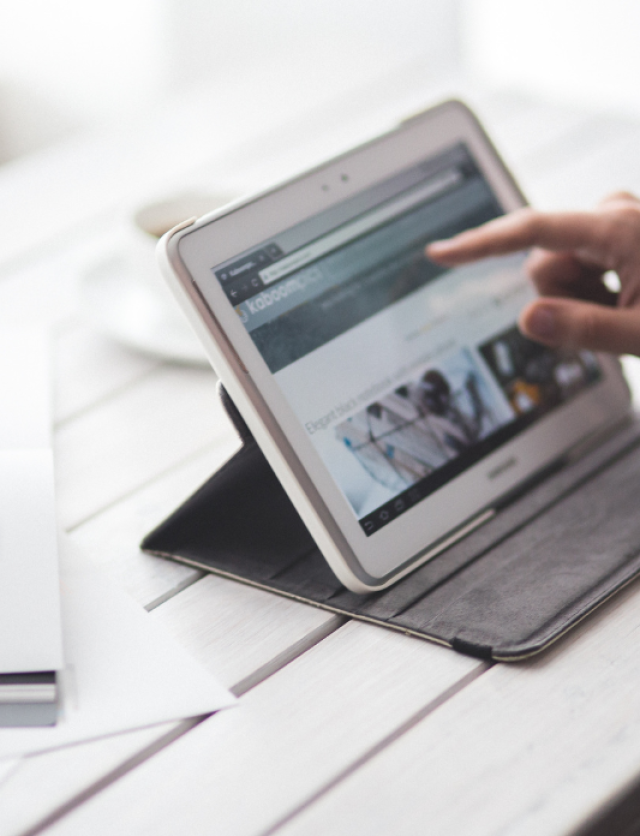 A hand browsing on a tablet placed on a table.